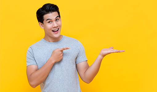 2023_0421_JACL_Static_Slider_Image_510x300_GuyYellowBkgrnd-1 Happy young man pointing to his left.